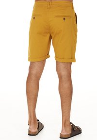 Gula bomullsshorts med rak silhuett, uppvikta fållar, två bakfickor med knäppning och en texturerad yta.