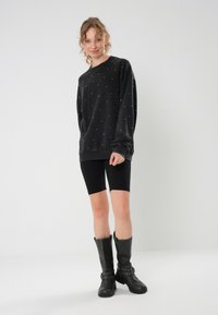 Felpa nera con punti argentati, vestibilità comoda, maniche lunghe; abbinata a pantaloni da bicicletta neri e stivali neri fino al ginocchio con accenti borchiati.