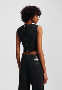 Top din denim negru, croppat, cu un guler înalt și fără mâneci, având o fermoar vizibil pe spate și o textură netedă.