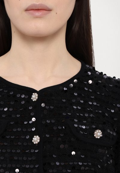Cardigan negru din paiete cu o suprafață texturată, având un guler rotund și nasturi decorativi accentuați cu perle pe față.