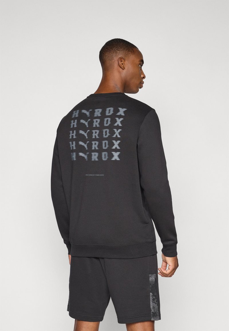 Black sweatshirt with a round neck, featuring a repeated graphic design on the back. Material is soft with a textured finish.
