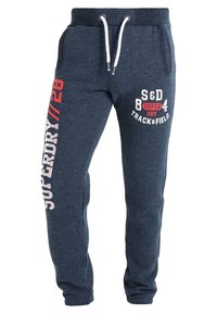 Navy blauwe joggerbroeken van een zachte stof, met witte trekkoorden, zijzakken en grote grafische prints in rood en wit.