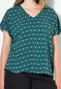 Blouse teal à col en V avec un motif en diamant en teal plus foncé. Coupe loose avec des manches courtes et un ourlet arrondi. Texture de tissu lisse.