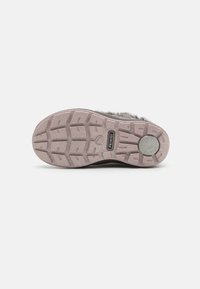 Semelle de chaussure en caoutchouc noir avec un motif de bande de roulement texturé et des accentuations gris clair. Présente un logo circulaire et des rainures pour l'adhérence et la traction.