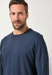 Camisa de manga larga azul marino con cuello redondo, hecha de un tejido suave. Presenta un ajuste relajado y costuras mínimas para mayor comodidad.