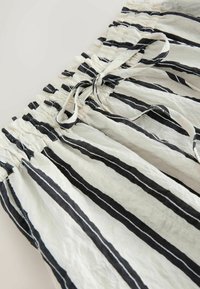 Weißer Stoff mit vertikalen schwarzen Streifen, mit einem gerafften elastischen Bund und einem gebundenen Kordelzug.