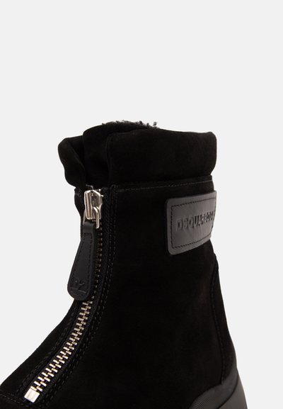 Bottine en daim noir avec fermeture éclair argentée à l'avant et écusson logo en cuir noir sur le côté affichant la marque "DSQUARED2".
