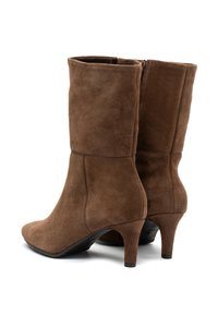 Ett par bruna mockastövlar i knähöjd med spetsiga tår, sidodragkedjor och smala kitten heels vinklade på vit bakgrund.