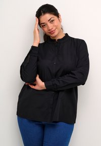 Sort button-up skjorte med en rynket krave og manchetter, der har en løs pasform og en glat tekstur, kombineret med blå denim jeans.