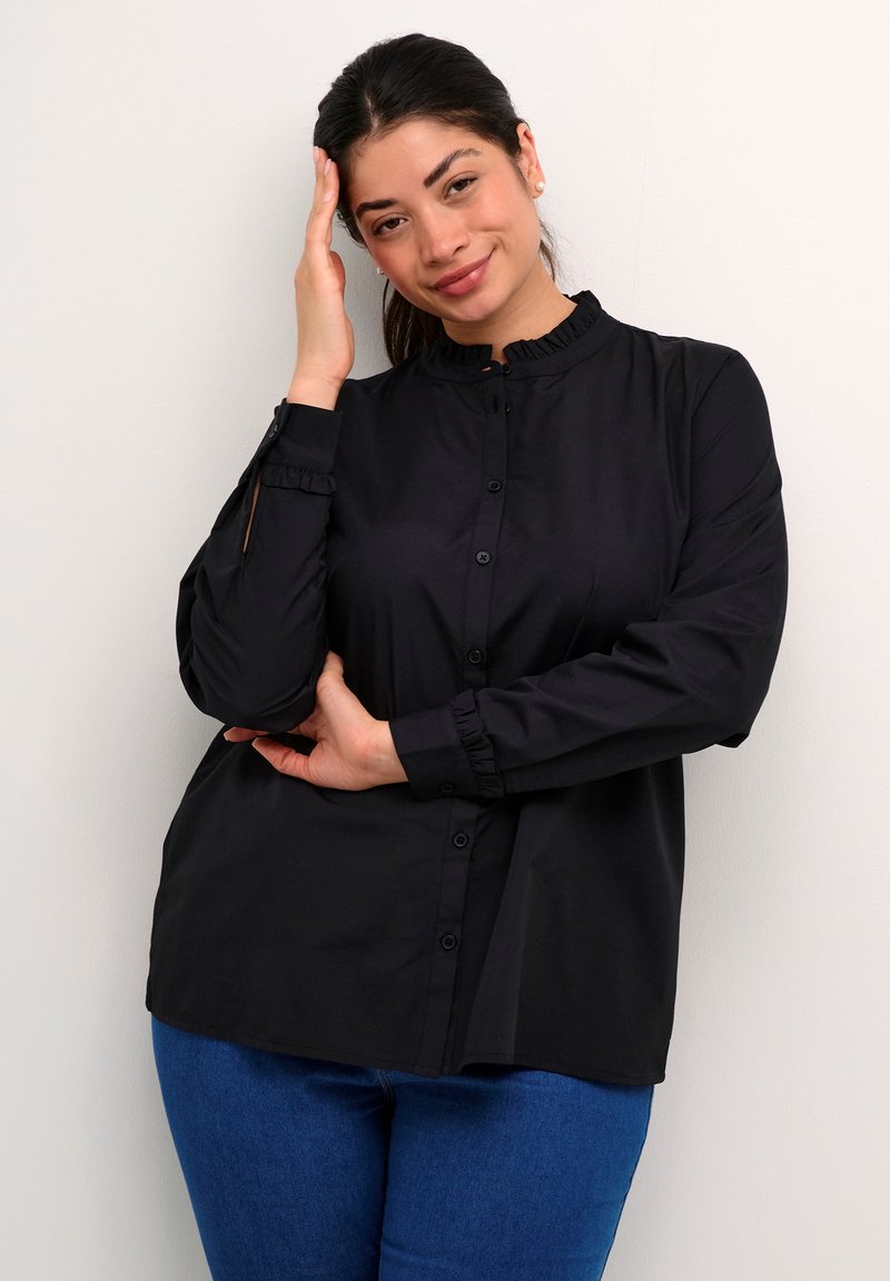 Schwarze Hemd mit Knopfleiste, einem Rüschenausschnitt und Rüschenmanschetten, mit lockerer Passform und glatter Textur, kombiniert mit blauen Jeans.