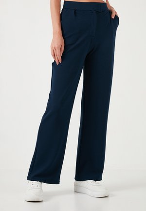 Navy blue wide-leg pants in a soft, stretchy fabric, featuring a drawstring waist and side pockets, paired with white sneakers.