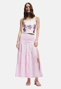 Valkoinen crop-top, jossa on kukkakoristeita; vaaleanpunainen kerroksellinen maxi-hame, jossa on sivuaukko; sileä kangas, jossa on ruudullinen kuvio; sandaalit.