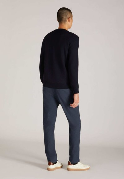 Marineblauer Pullover mit gerippten Bündchen und Saum, kombiniert mit dunkelblauen Hosen und weißen Turnschuhen mit braunen Akzenten. Rückansicht dargestellt.