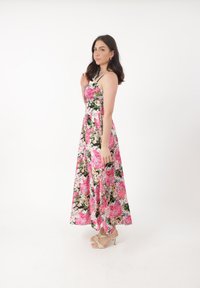 Blomster maxi kjole med et levende mønster i pink, grøn og hvid, med tynde stropper og en svajende silhuet. Båret med beige hæle.
