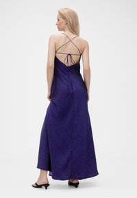 Langes violettes Maxikleid mit weißen Punkten, verstellbaren gekreuzten Trägern und einer Schnürung am Rücken. Glatter Stoff mit fließendem Design.