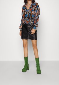 Blouse à manches longues fleurie avec des motifs bleus, orange et beiges. Associée à une mini-jupe en cuir noir et des bottines à talons carrés en suède vert.