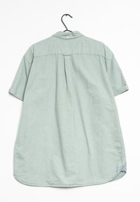 Lichtgroen, kort mouwenshirt van zacht materiaal, met een knoopsluiting kraag, een achterste plooi en een gebogen zoom. Hangend aan een zwarte haak.