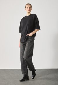 Maglietta nera oversize a maniche corte, abbinata a jeans grigi scuri a vita alta con gamba dritta e stivali neri con tacco alla caviglia.