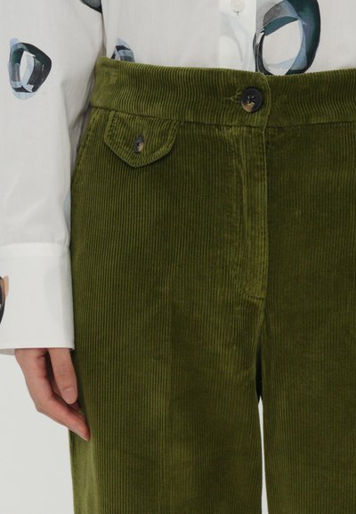 Pantalones de pana verde oliva con acabado texturizado, que presentan un cierre frontal con botón y un pequeño bolsillo con solapa en la cinturilla.