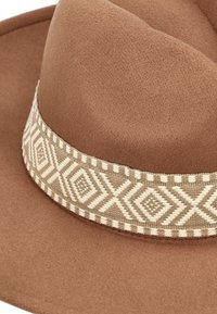 Bruine vilt hoed met een decoratieve geweven band met een geometrisch crèmekleurig patroon. Het ontwerp heeft een platte rand en een ronde kroon.