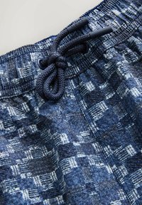 Šortky so šnúrkou v páse z modrej tkaniny s geometrickým vzorom a kontrastnými svetlejšími akcentmi, s čiernymi plastovými detailmi.
