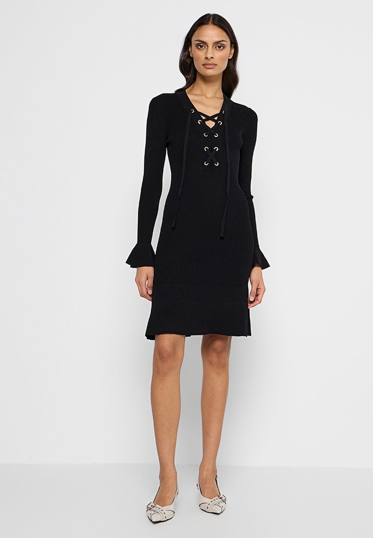 Czarna dzianinowa sukienka prążkowana z długimi rękawami, dekoltem z wiązaniem z złotymi oczkami i rozszerzanymi mankietami, sięgająca do połowy uda.