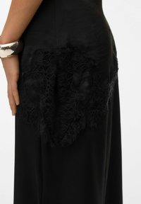 Vestido negro con una textura sedosa y un intrincado detalle de encaje negro en un lado, con un diseño ajustado y suave y una silueta fluida.