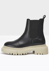 Black leather Chelsea boots with elastic side panels, thick beige rubber soles, and a tab on the back for easy pull-on.