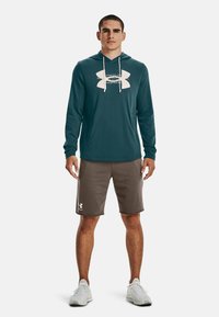 Felpa con cappuccio verde acqua con logo bianco, abbinata a pantaloni corti grigi con logo e scarpe da ginnastica chiare. Combinazione di abbigliamento atletico casual.