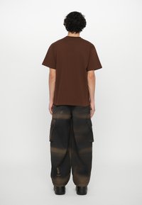 Brown cotton t-shirt with short sleeves, paired with cargo pants in shades of black and brown, featuring pockets and a relaxed fit.