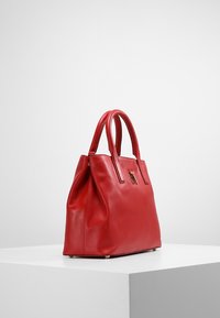 Sac à main en cuir rouge avec une texture lisse, deux poignées et une forme rigide. Présente des éléments en métal doré à l'avant pour le détail.