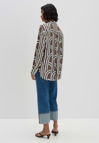 Braun-weißt gestreiftes Hemd mit langen Ärmeln, Knopfdetails, kombiniert mit weiten blauen Jeans mit umgeschlagenem Saum.