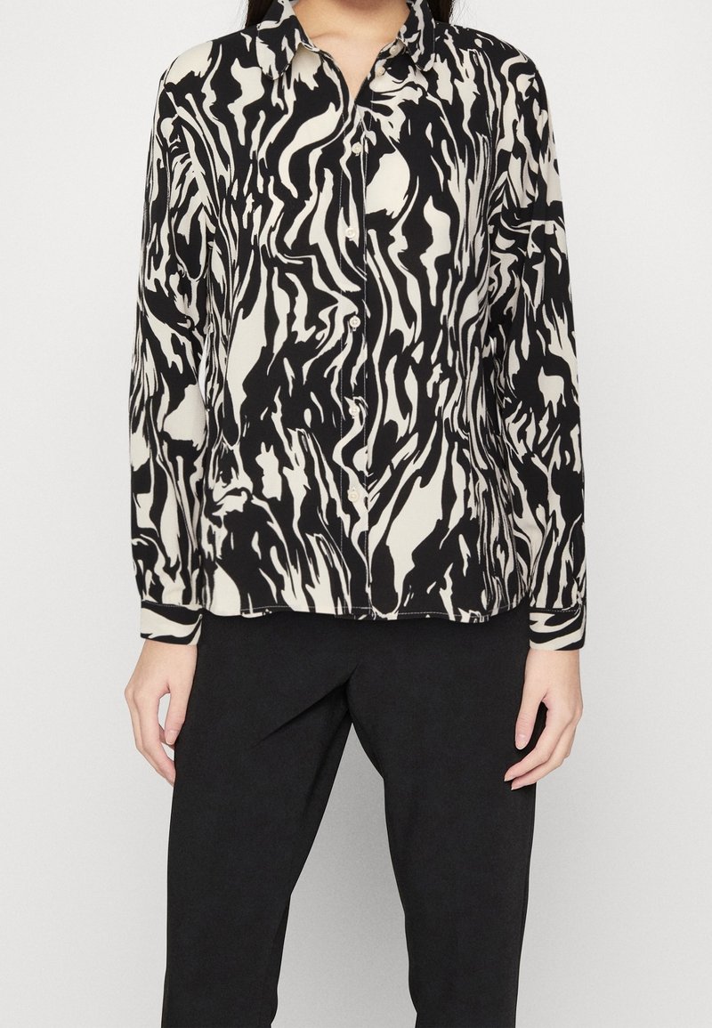 Blusa de manga larga en negro y crema con un patrón abstracto de olas. Presenta un cuello clásico y cierre de botones, hecha de una tela suave.