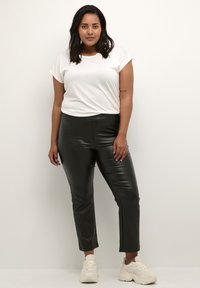 Weißes Kurzarm-T-Shirt kombiniert mit schwarzen, enganliegenden Hosen aus Kunstleder, die eine glatte Textur und eine Knöchellänge aufweisen, ergänzt durch helle Sneakers.