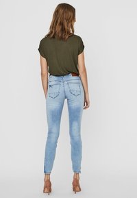 Úzké džíny ve světle modré denimové barvě s jemným vyblednutím, doplněné tmavě zeleným tričkem s krátkým rukávem. Obsahují dvě zadní kapsy a rozparky na kotnících.