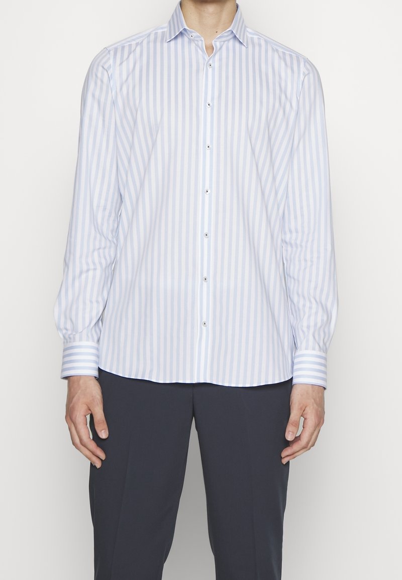 Koszula zapinana na guziki w białe i jasnoniebieskie paski. Ma długie rękawy i spiczasty kołnierzyk. Wykonana z gładkiej tkaniny o miękkiej fakturze.