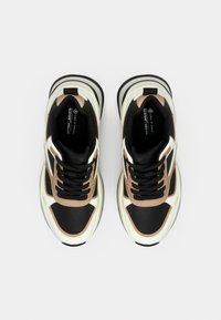 Μαύρα και μπεζ αθλητικά παπούτσια με υφασμάτινο επάνω μέρος, λευκές λεπτομέρειες και χοντρή μαύρη σόλα. Διαθέτουν στρογγυλά κορδόνια και λογότυπο στη γλώσσα.