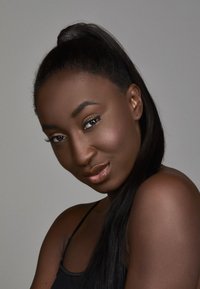 Portrait d'une personne avec de longs cheveux noirs coiffés en une haute queue de cheval, une peau lisse et brunâtre, un maquillage subtil et un haut noir sur fond gris.