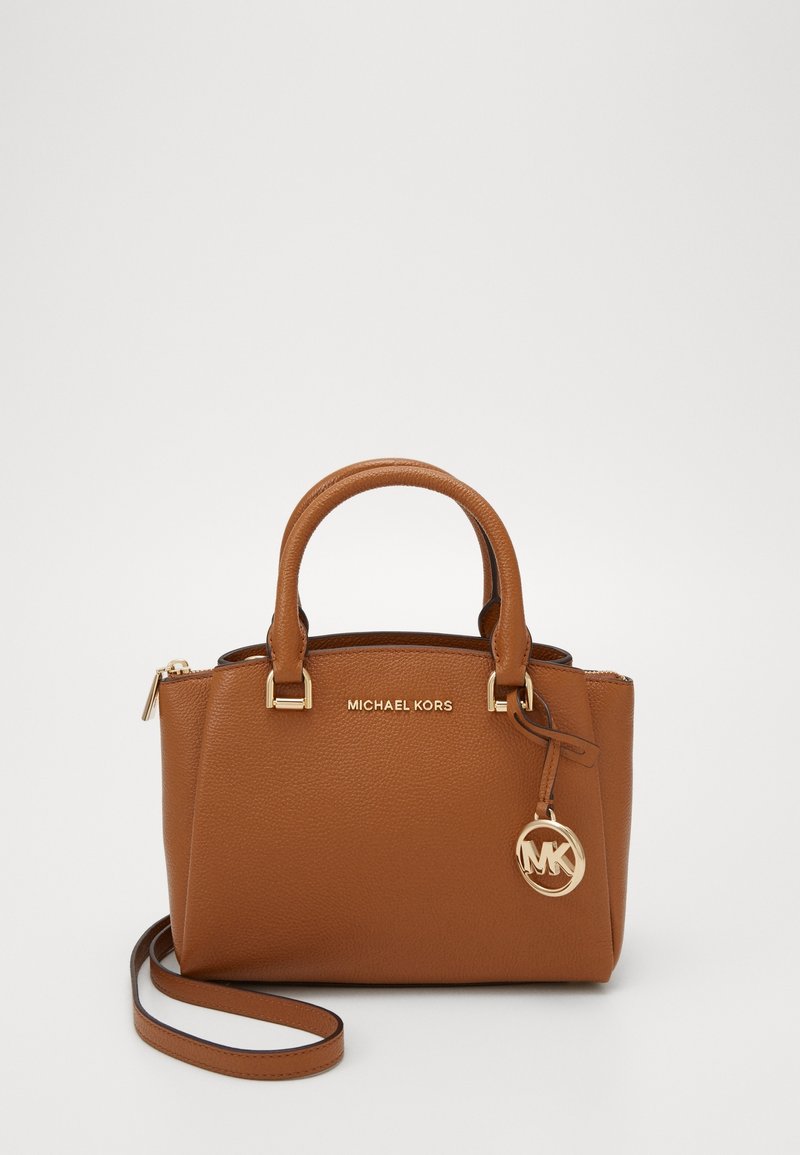 Sac à main en cuir marron Michael Kors avec double poignée, une bandoulière amovible et un charm avec logo MK doré suspendu sur le côté.
