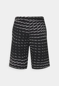 Pantaloni corti neri con loghi "adidas" bianchi e motivi a trifoglio disposti in linee curve su uno sfondo chiaro e uniforme.