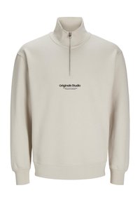 Suéter beige con un alto cuello y cremallera de cuarto, que presenta un logo negro "Originals Studio" en la parte frontal, puños y dobladillo acanalados.