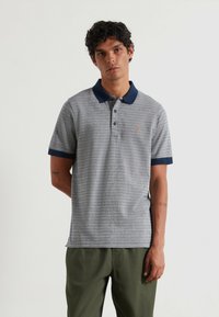 Polo a righe grigie con colletto e maniche blu navy, caratterizzato da un piccolo logo ricamato sul petto. Tessuto misto cotone.