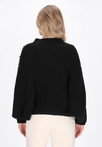 Maglione nero in maglia con texture a costine, caratterizzato da un colletto alto e maniche a sbuffo, con bottoni decorativi lungo le cuciture delle spalle.