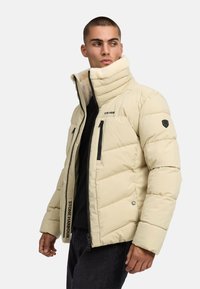 Puhasta jakna u svijetloj bež boji s visokim ovratnikom, crnim zatvaračima na džepovima i "STONE HARBOUR" brandingom sprijeda. Mekana unutarnja podstava.