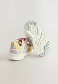 Ett par barnskor i pastellfärger med rosa, beige och grå detaljer; den ena skon visar sin mönstrade vita sula.