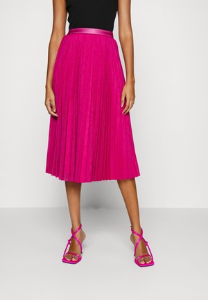 Plisovaná, midi sukně v jasně růžové barvě s páskem ze saténu; v kombinaci s teniskami na tenkých páscích a hranatou špičkou ve stejné barvě.