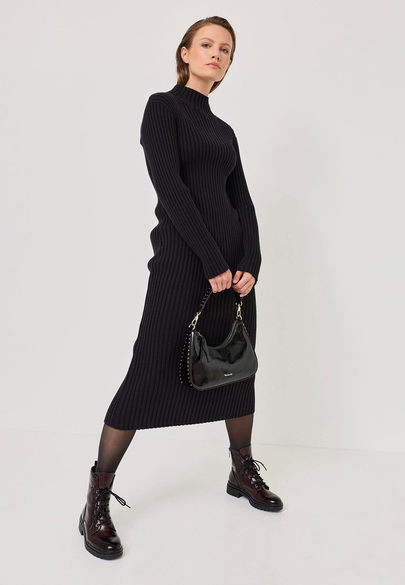 Schwarzes, geripptes Strickkleid mit hohem Kragen, kombiniert mit einer glänzenden, schwarzen Handtasche und burgunderfarbenen, schnürbaren Kampfstiefeln. Glattes Material und schlanke Silhouette.