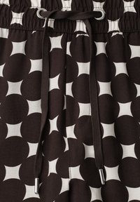 Tissu à motifs noir et blanc avec un cordon passant à travers des œillets métalliques sur une ceinture froncée.