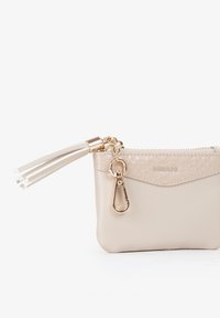 Piccola borsa beige con cerniera, parte superiore testurizzata, dettagli in oro e un accentuato nappina bianca. Dotata di una chiusura a moschettone per l'aggancio.