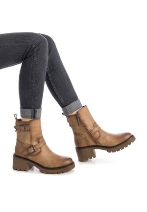 Botas de cuero marrón hasta el tobillo con un tacón grueso, aseguradas por dos hebillas ajustables y un cremaller lateral, con una suela de goma texturizada.